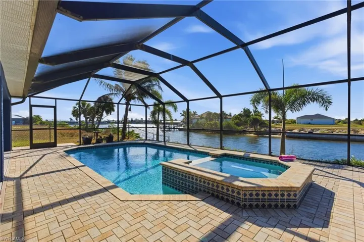 Integrated pool / spa with a sunroom, glass enclosure, a water view, and a patio