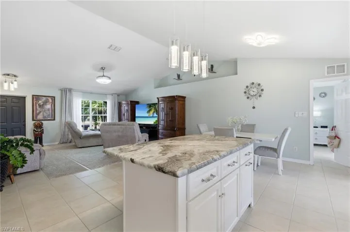 Kitchen featuring white cabinets, open floor plan, light tile patterned flooring, lofted ceiling, and a kitchen island