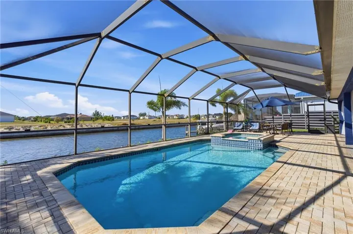 Combined pool / hot tub featuring a sunroom, a water view, glass enclosure, and a patio area