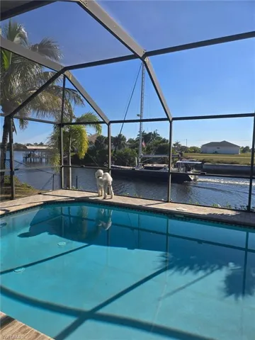 Outdoor pool with glass enclosure, a sunroom, and a water view