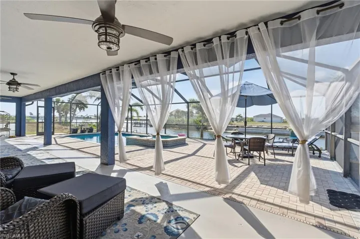 View of patio with ceiling fan, a sunroom, outdoor dining area, a pool with connected hot tub, and glass enclosure