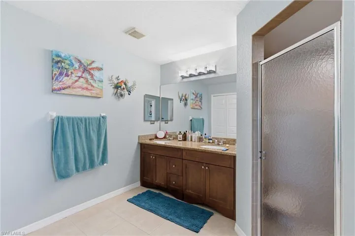 Full bath with double vanity, a shower stall, and light tile patterned flooring