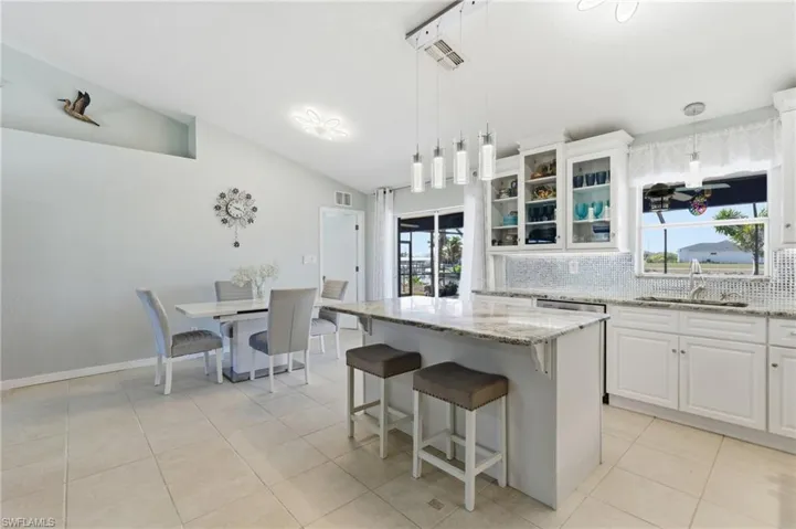 Kitchen featuring white cabinetry, glass insert cabinets, light stone countertops, backsplash, and hanging light fixtures