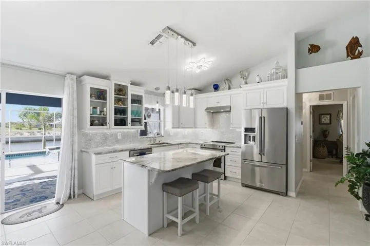 Kitchen featuring stainless steel appliances, glass insert cabinets, vaulted ceiling, white cabinets, and a kitchen breakfast bar