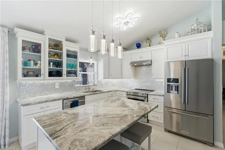 Kitchen with stainless steel appliances, glass fronted cabinets, vaulted ceiling, and white cabinets