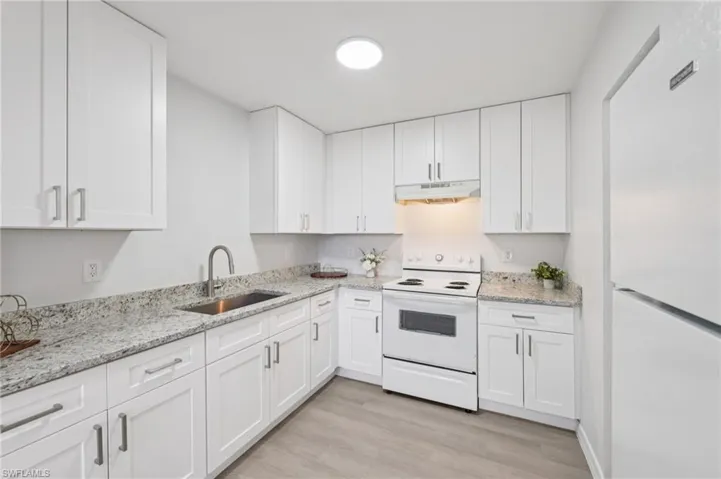 Kitchen with white appliances, light stone countertops, white cabinets, and light wood-type flooring