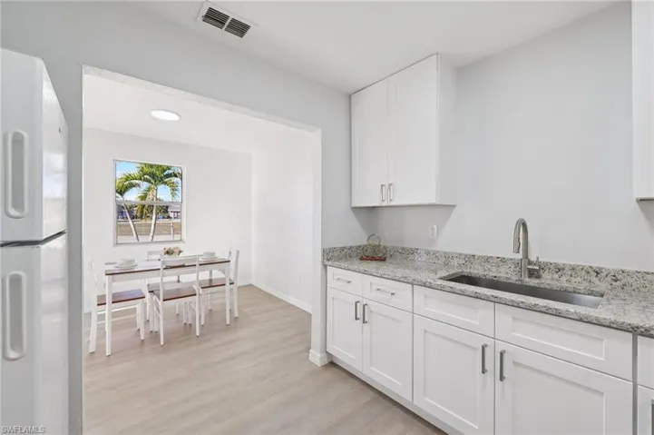 Kitchen with white cabinetry, light stone counters, freestanding refrigerator, and light wood finished floors