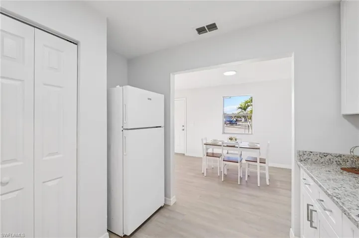 Kitchen with freestanding refrigerator, white cabinets, light stone countertops, and light wood-style flooring