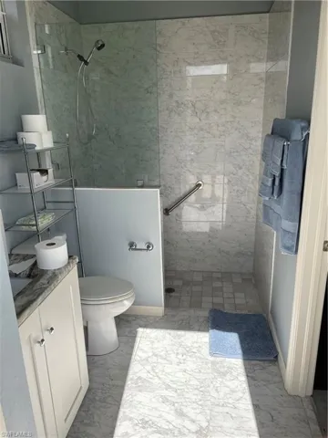 Bathroom featuring tile flooring, tiled shower, toilet, and vanity
