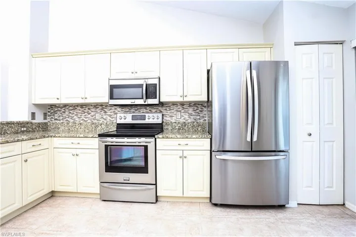 Kitchen with stainless steel appliances, tasteful backsplash, light stone countertops, cream cabinetry, and lofted ceiling