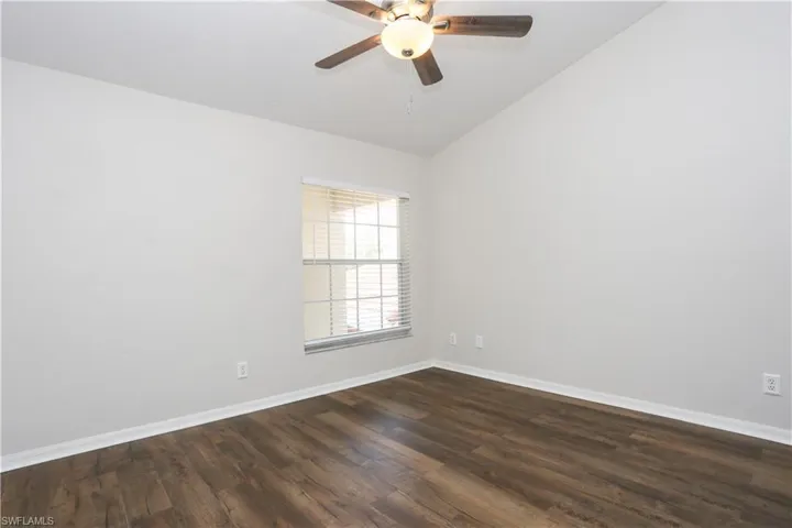 Empty room featuring baseboards, dark wood finished floors, lofted ceiling, and ceiling fan