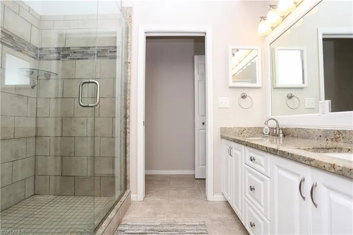 Full bathroom featuring a stall shower, double vanity, tile patterned flooring, and baseboards
