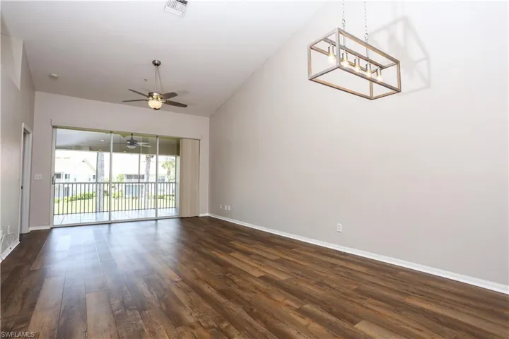 Spare room with dark wood finished floors, baseboards, a chandelier, ceiling fan, and lofted ceiling