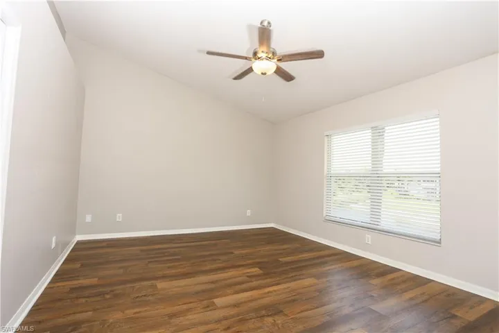 Unfurnished room with lofted ceiling, ceiling fan, dark wood-type flooring, and baseboards