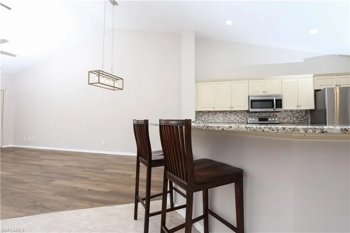 Kitchen featuring stainless steel appliances, a kitchen breakfast bar, high vaulted ceiling, decorative backsplash, and pendant lighting