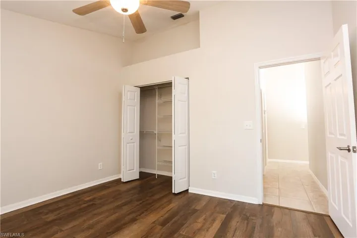 Unfurnished bedroom with dark wood-style flooring, a towering ceiling, baseboards, a closet, and ceiling fan