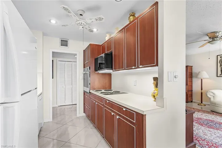 Kitchen with ceiling fan, white appliances, light countertops, and bold wood finish cabinetry