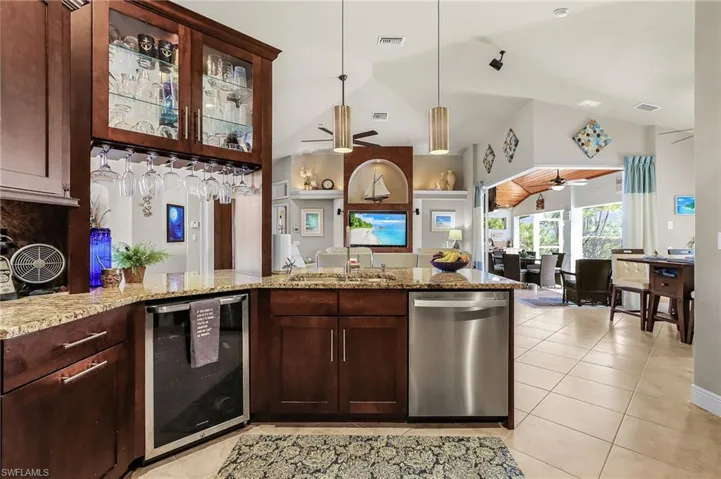 Kitchen featuring dishwasher, dark wood finish cabinetry, light stone countertops, and lofted ceiling
