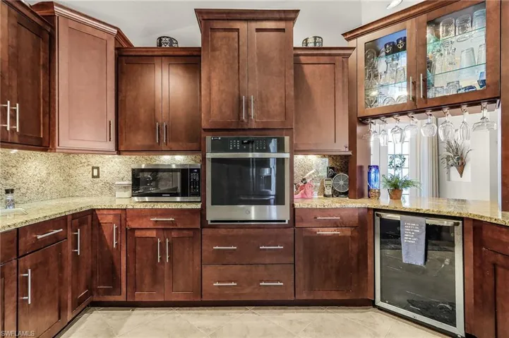 Kitchen with wine cooler, stainless steel appliances, light stone countertops, and decorative backsplash