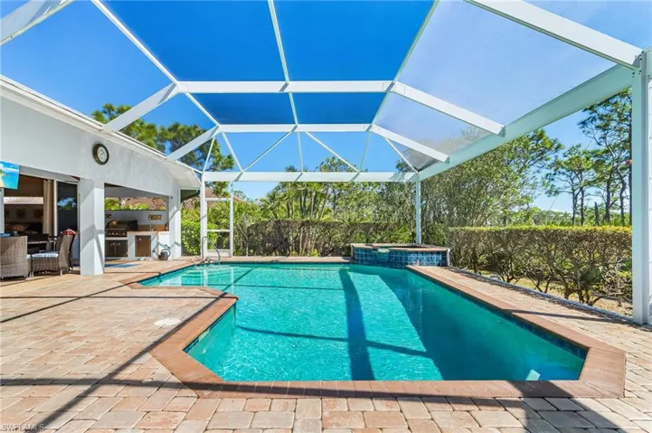Outdoor pool with a patio, exterior kitchen, glass enclosure, a sunroom, and a hot tub