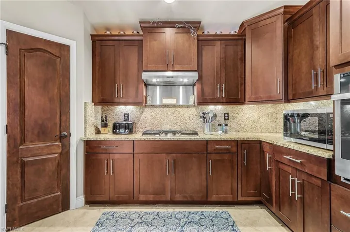 Kitchen with backsplash, light stone countertops, stainless steel appliances, and light tile patterned floors