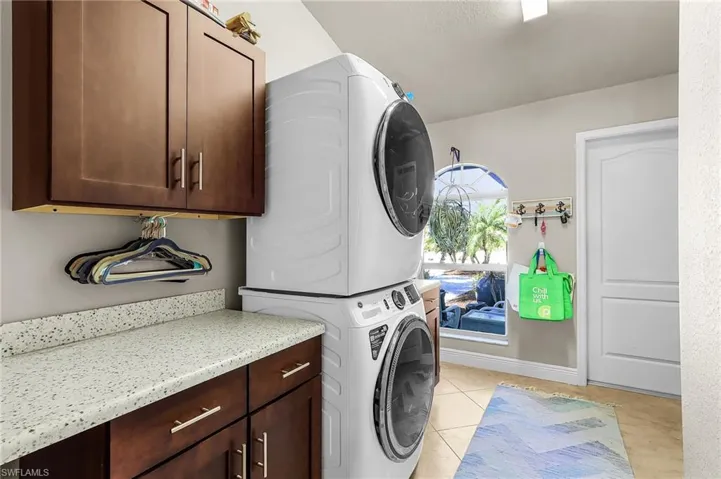 Laundry area featuring stacked washing machine and dryer, light tile patterned flooring, and cabinet space
