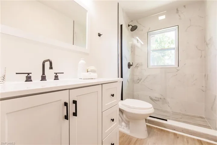 Bathroom featuring tiled shower, vanity, toilet, and hardwood / wood-style floors