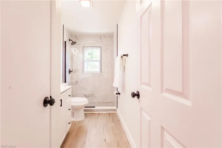 Bathroom featuring tiled shower, hardwood / wood-style flooring, toilet, and vanity