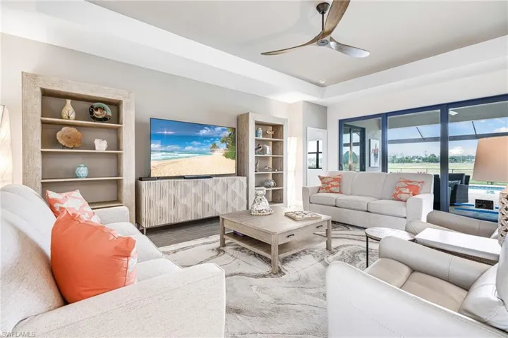 Living area with a ceiling fan, a tray ceiling, built in shelves, and wood finished floors