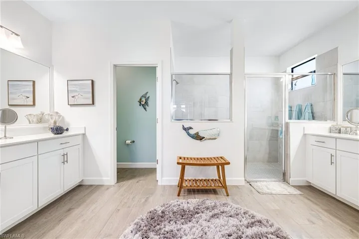 Full bathroom featuring a stall shower, baseboards, two vanities, and wood finished floors