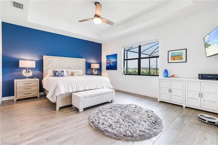 Bedroom with a tray ceiling, light wood-type flooring, visible vents, and baseboards
