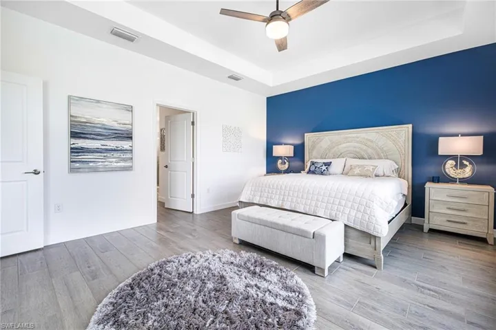 Bedroom featuring baseboards, visible vents, a raised ceiling, ceiling fan, and wood finished floors