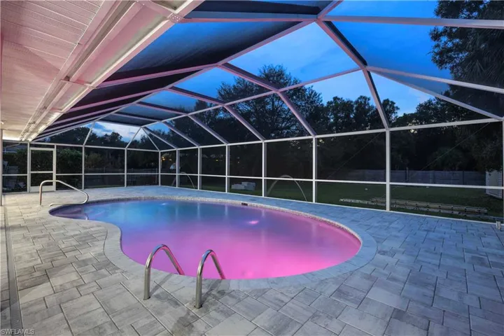 Swimming pool with glass enclosure, a sunroom, a patio, and view of wooded area
