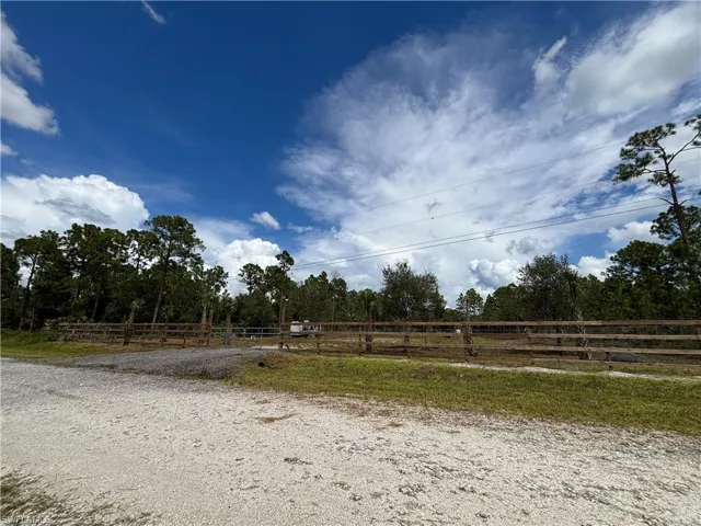 Gravel driveway leading to a wooden fence, bordered by mature trees and natural landscaping