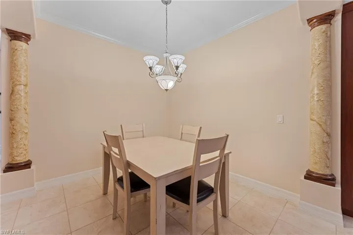 Dining room with light tile patterned floors, a notable chandelier, ornamental molding, and ornate columns