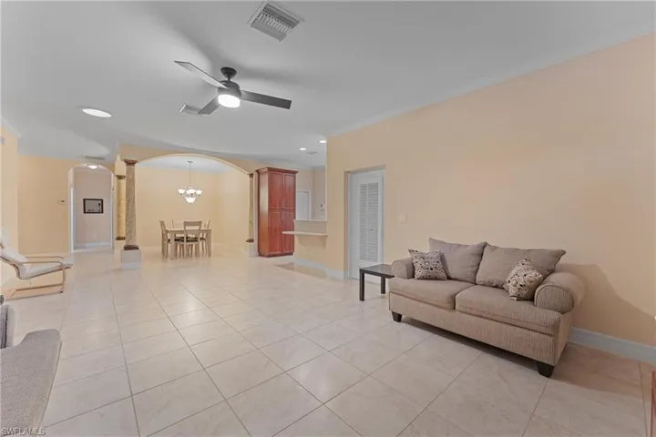 Tiled living room with crown molding and ceiling fan with notable chandelier