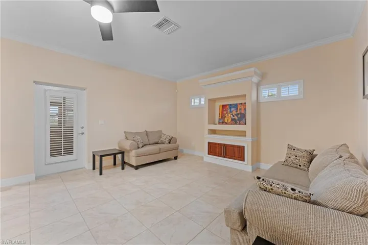 Living room with ceiling fan, built in shelves, light tile patterned floors, and crown molding