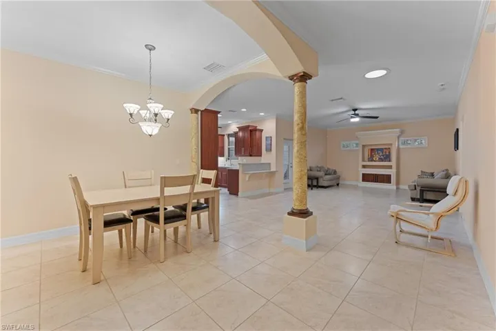 Dining space with light tile patterned floors, ceiling fan with notable chandelier, ornamental molding, and ornate columns