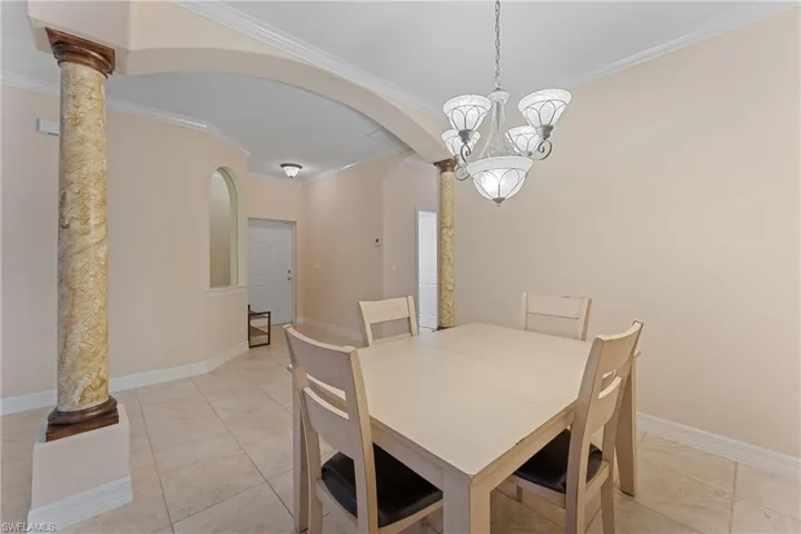 Tiled dining area with decorative columns, crown molding, and a notable chandelier