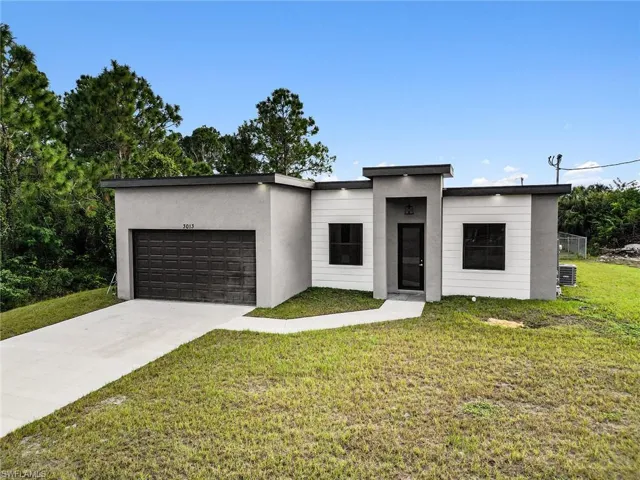 Modern home with a front lawn, a garage, driveway, and stucco siding