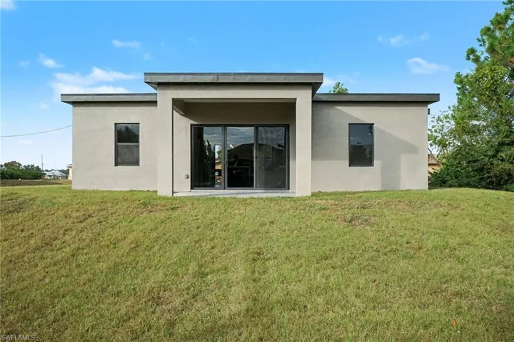 Back of house with a lawn and stucco siding