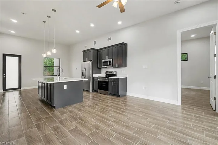 Kitchen featuring stainless steel appliances, a kitchen island with sink, ceiling fan, wood finish floors, and decorative light fixtures