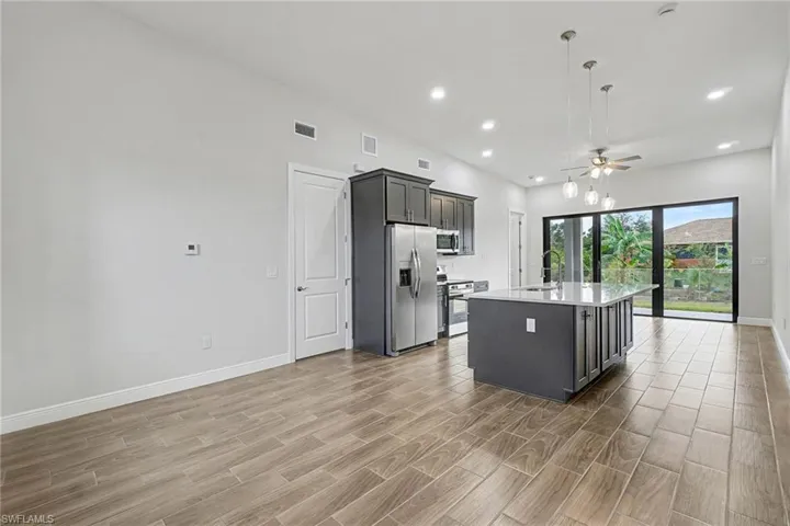 Kitchen featuring hanging light fixtures, an island with sink, wood tiled floors, a ceiling fan, and stainless steel appliances