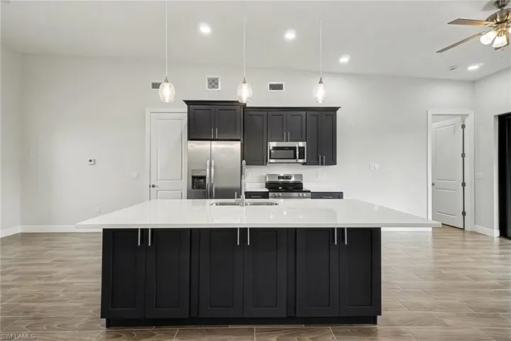 Kitchen featuring stainless steel appliances, dark cabinets, wood finish floors, a center island with sink, and light stone countertops