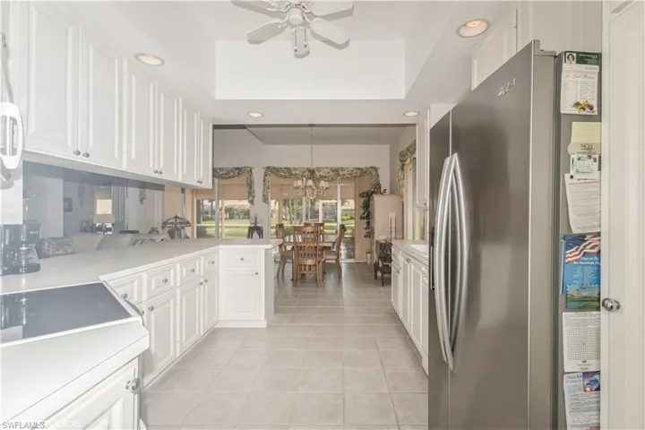 Kitchen with stainless steel refrigerator, ceiling fan with notable chandelier, a tray ceiling, white cabinetry, and light tile floors