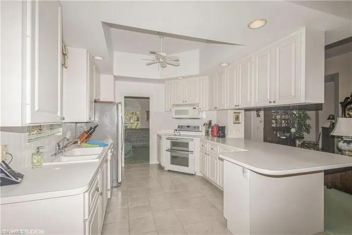 Kitchen with kitchen peninsula, ceiling fan, a tray ceiling, white cabinetry, and white appliances