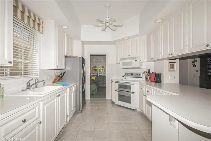 Kitchen featuring white appliances, light tile flooring, backsplash, sink, and white cabinetry