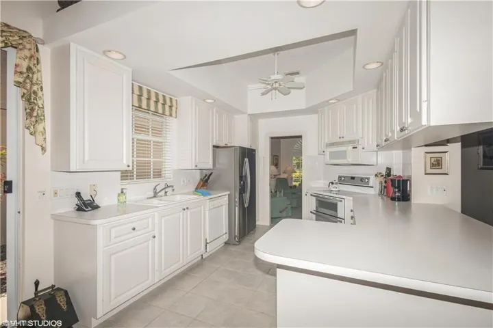 Kitchen with sink, kitchen peninsula, white cabinets, and white appliances