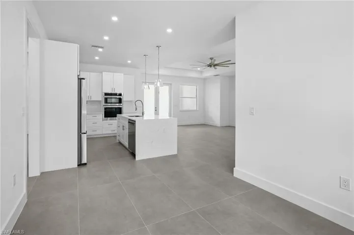 Kitchen with hanging light fixtures, white cabinetry, light tile patterned floors, light stone countertops, and ceiling fan