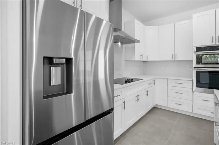 Kitchen with stainless steel appliances, decorative backsplash, wall chimney exhaust hood, white cabinetry, and light tile patterned flooring
